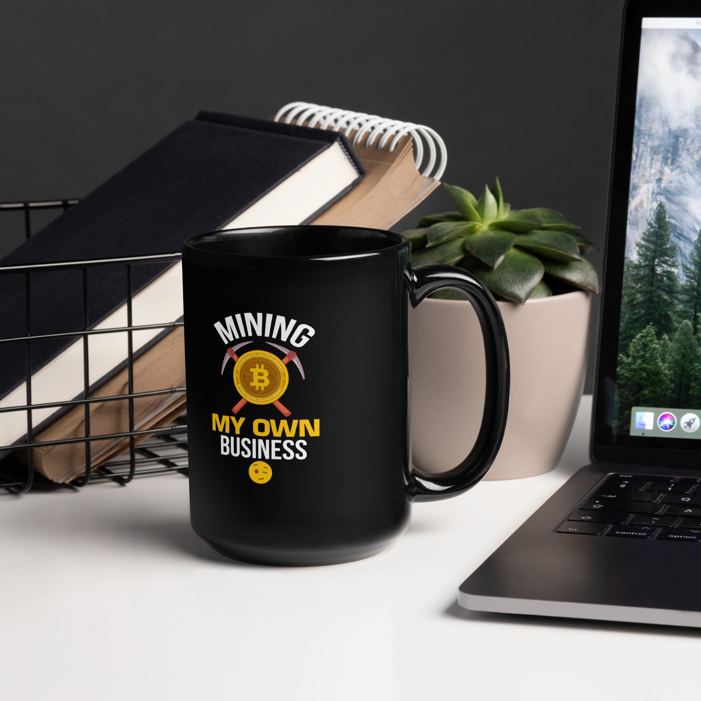 15 oz black coffee mug featuring “Mining My Own Business” crypto design, styled on office desk with books, plant, and laptop.