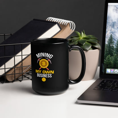 15 oz black coffee mug featuring “Mining My Own Business” crypto design, styled on office desk with books, plant, and laptop.